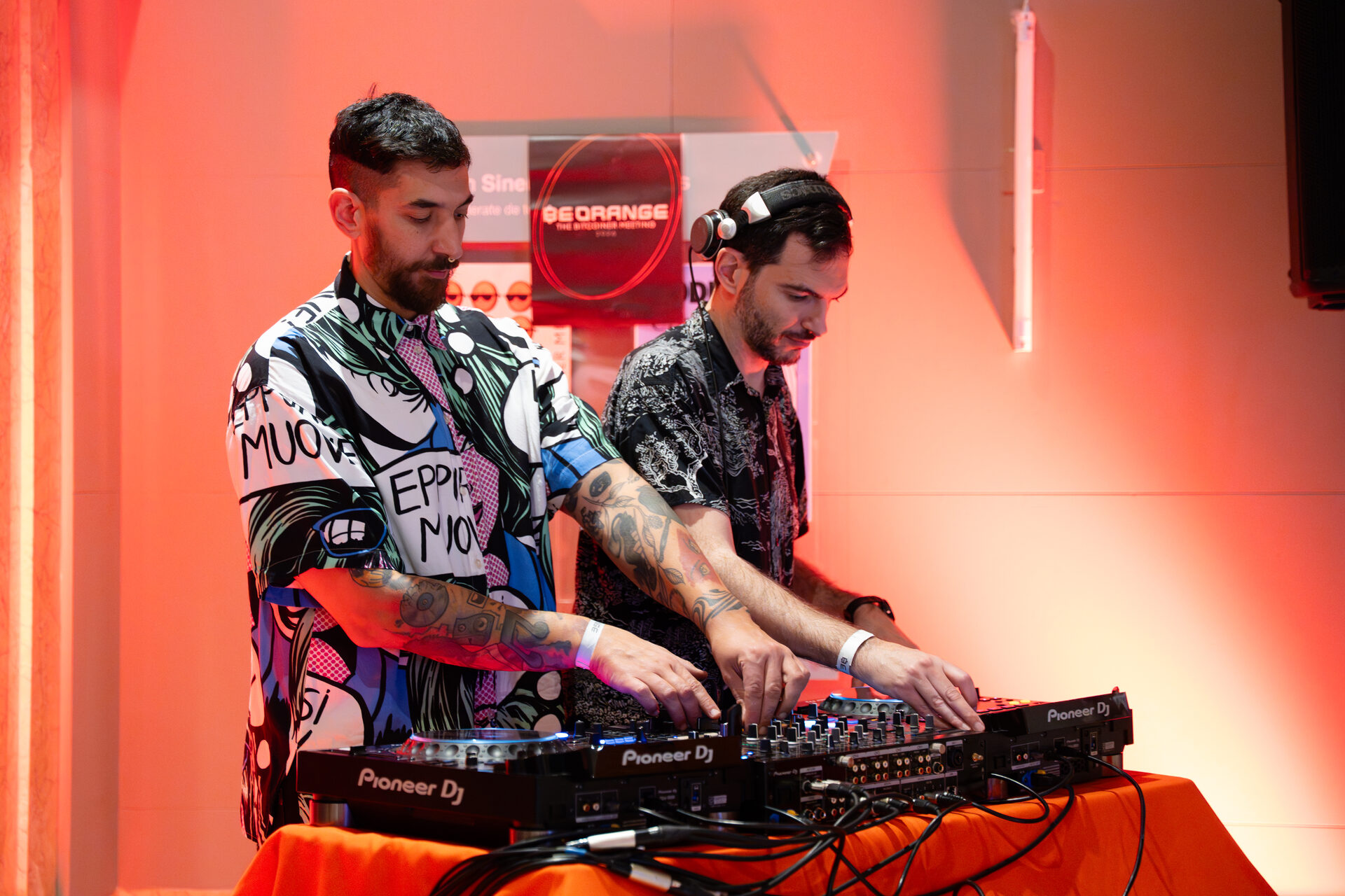 Dos DJs mezclan en vivo bajo luces rojas en Be Orange.