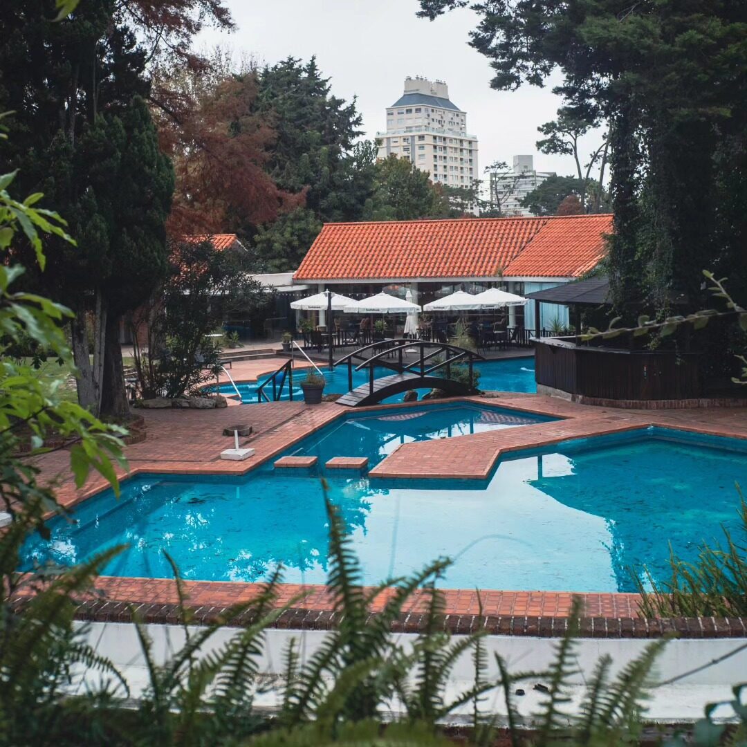 Piscina y jardín del venue durante el día, con el edificio de techo rojo de fondo.